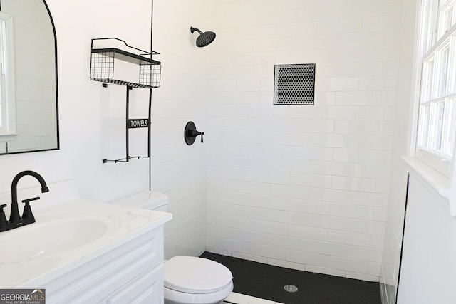 bathroom featuring toilet, tiled shower, and vanity