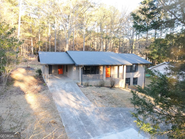 ranch-style home featuring covered porch, an attached carport, concrete driveway, and roof with shingles