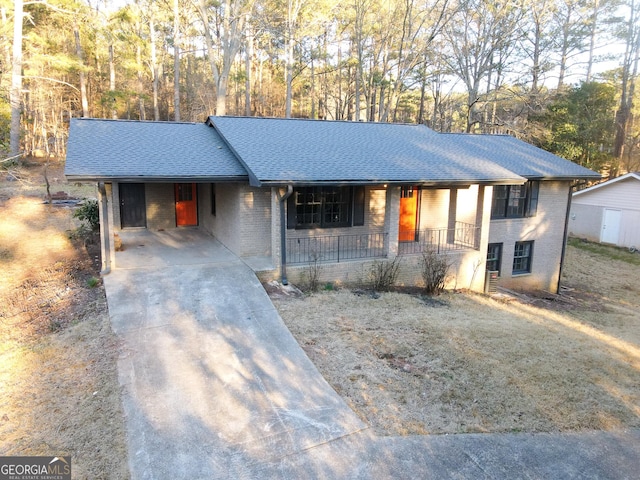 single story home with a porch, an attached carport, brick siding, a shingled roof, and concrete driveway