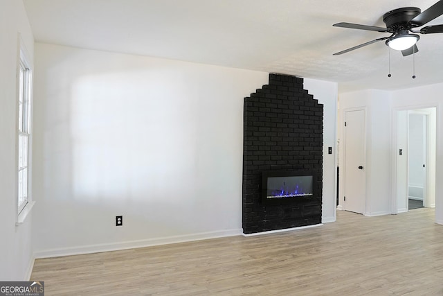 unfurnished living room with a brick fireplace, ceiling fan, baseboards, and light wood-style floors