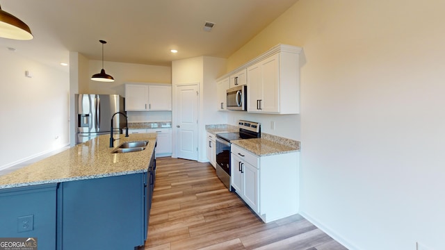 kitchen with stainless steel appliances, a sink, white cabinetry, an island with sink, and decorative light fixtures