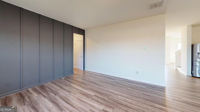 unfurnished room featuring light wood-type flooring, visible vents, and baseboards