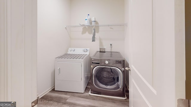 clothes washing area featuring laundry area, washer and clothes dryer, wood finished floors, and baseboards