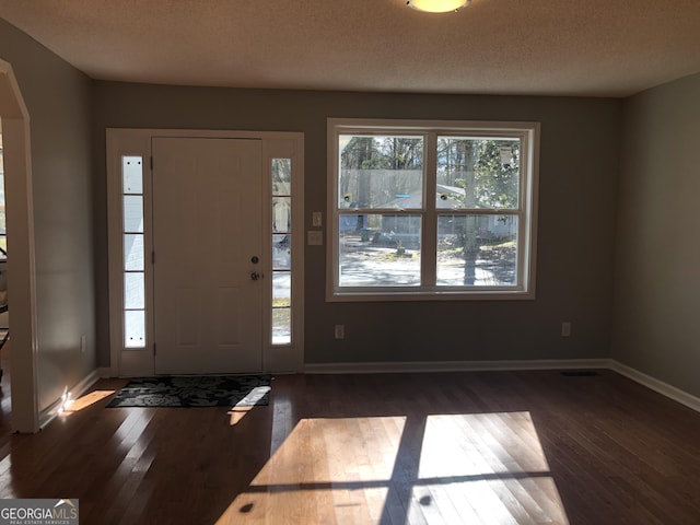 foyer entrance featuring a healthy amount of sunlight, arched walkways, and dark wood finished floors