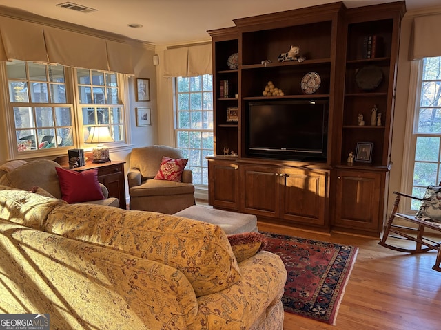 living room featuring light wood-type flooring, a healthy amount of sunlight, visible vents, and crown molding