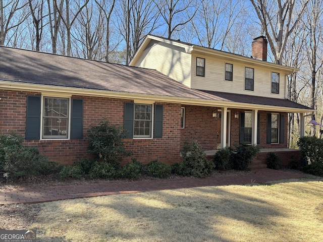 view of front of house featuring a porch, brick siding, a shingled roof, a front lawn, and a chimney