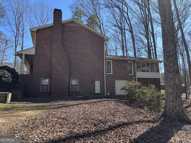 view of side of property featuring a sunroom, brick siding, and a chimney