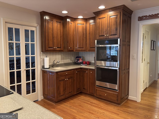 kitchen with light wood finished floors, light countertops, backsplash, stainless steel double oven, and a sink