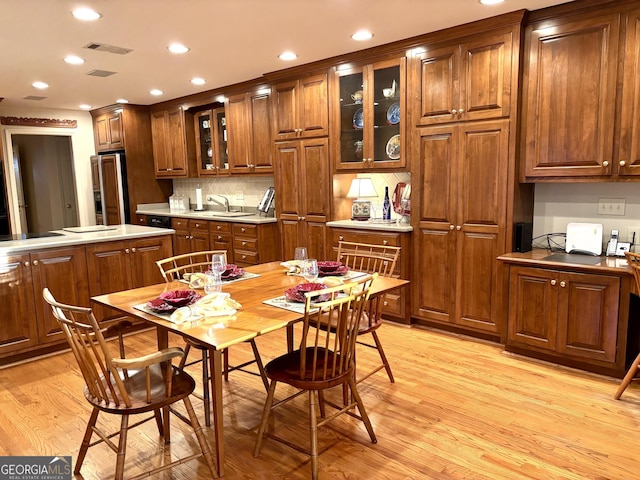 kitchen featuring light wood finished floors, visible vents, glass insert cabinets, brown cabinetry, and paneled fridge