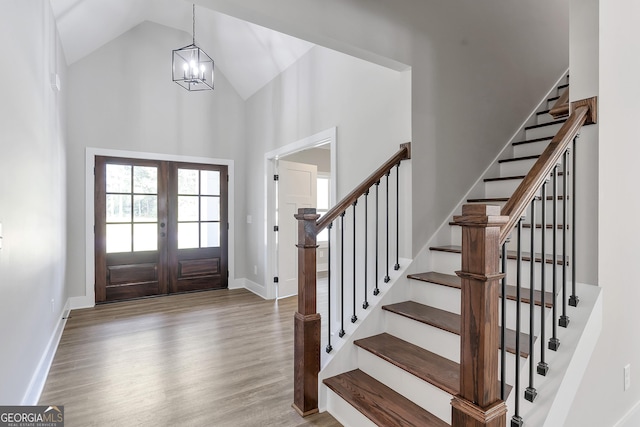 entrance foyer featuring an inviting chandelier, high vaulted ceiling, french doors, and hardwood / wood-style flooring