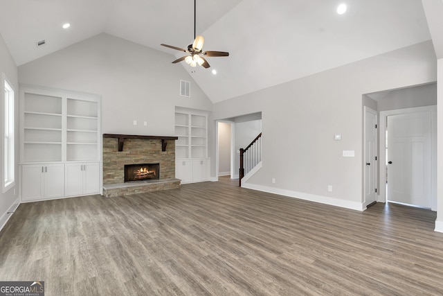 unfurnished living room with hardwood / wood-style flooring, built in shelves, a stone fireplace, ceiling fan, and high vaulted ceiling