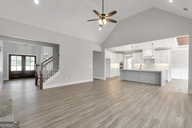 unfurnished living room with french doors, ceiling fan, high vaulted ceiling, sink, and light wood-type flooring