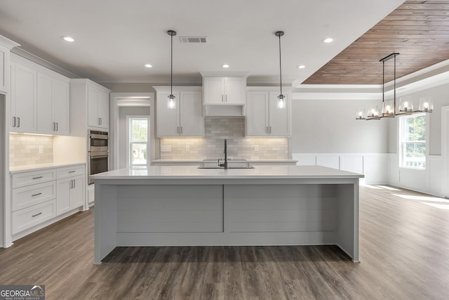 kitchen featuring double oven, white cabinets, decorative light fixtures, sink, and a kitchen island with sink