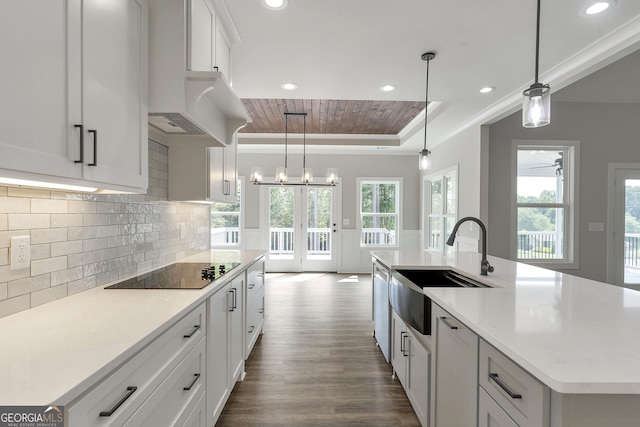 kitchen featuring a center island with sink, white cabinets, black electric cooktop, decorative light fixtures, and sink