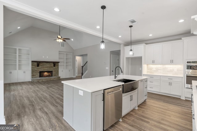 kitchen with stainless steel appliances, white cabinets, pendant lighting, sink, and a kitchen island with sink