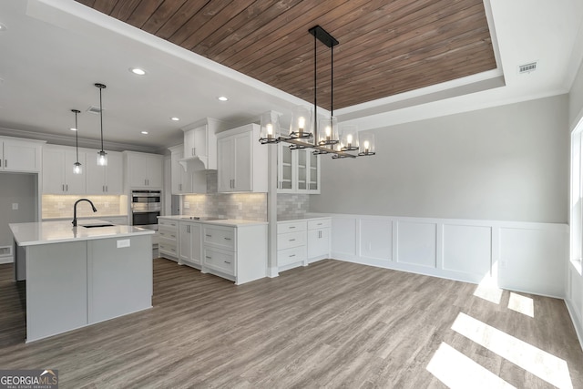 kitchen featuring a tray ceiling, pendant lighting, white cabinetry, and a center island with sink