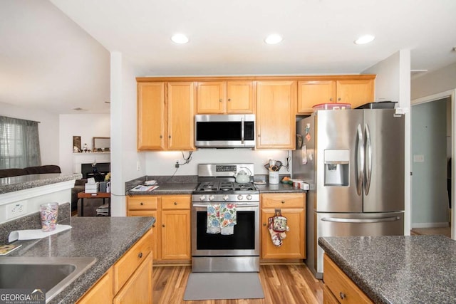 kitchen with appliances with stainless steel finishes, dark stone countertops, and light hardwood / wood-style floors