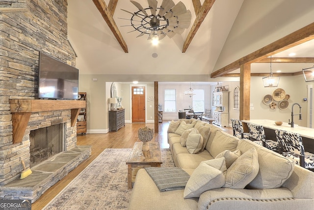 living room with a fireplace, beam ceiling, light hardwood / wood-style floors, ceiling fan, and high vaulted ceiling