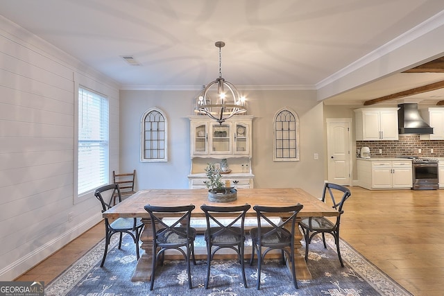 dining space featuring light wood-type flooring, crown molding, a notable chandelier, and beam ceiling