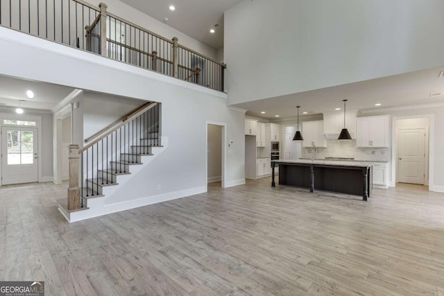 unfurnished living room featuring light wood-type flooring, ornamental molding, and a towering ceiling