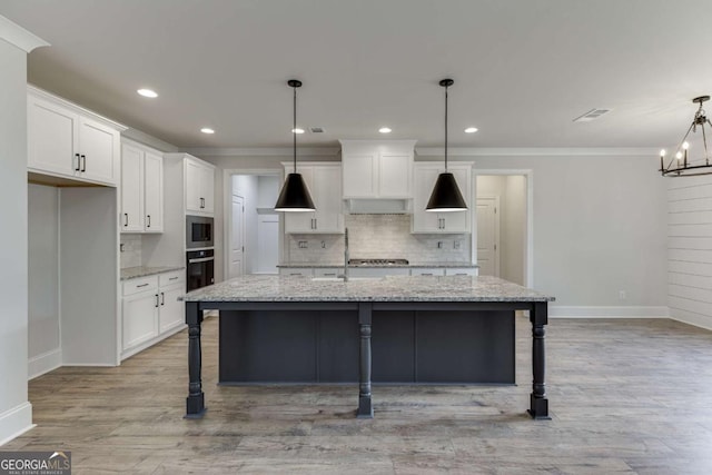 kitchen featuring white cabinetry, a center island with sink, light stone counters, appliances with stainless steel finishes, and pendant lighting