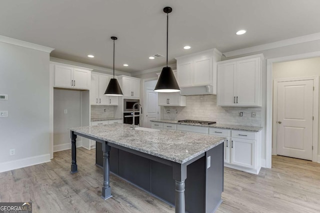 kitchen featuring stainless steel gas cooktop, a kitchen island with sink, light stone counters, white cabinets, and pendant lighting