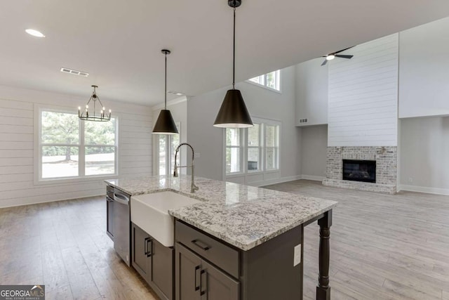 kitchen with sink, light wood-type flooring, dishwasher, decorative light fixtures, and a fireplace