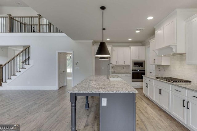 kitchen featuring stainless steel appliances, white cabinetry, hanging light fixtures, and wall chimney range hood