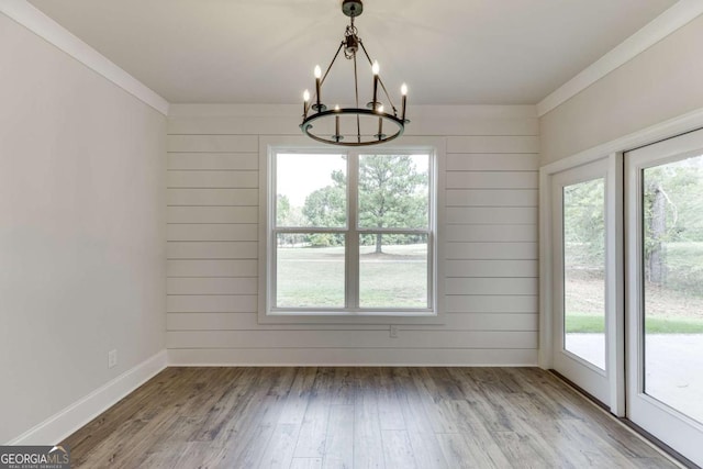 unfurnished dining area featuring hardwood / wood-style floors, crown molding, a chandelier, and plenty of natural light