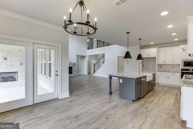 kitchen with a center island with sink, decorative light fixtures, backsplash, sink, and white cabinetry