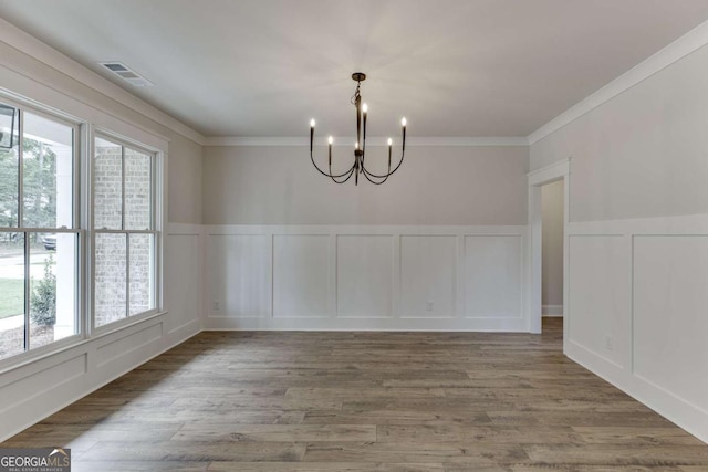 unfurnished dining area featuring an inviting chandelier, plenty of natural light, wood-type flooring, and ornamental molding