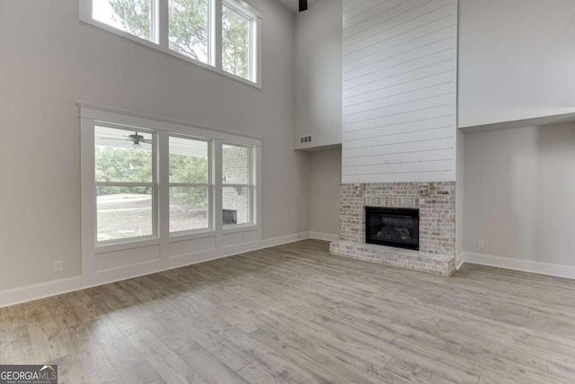 unfurnished living room with a brick fireplace, a towering ceiling, and light hardwood / wood-style flooring