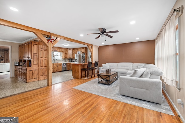 living room with sink, ornamental molding, light hardwood / wood-style floors, and ceiling fan