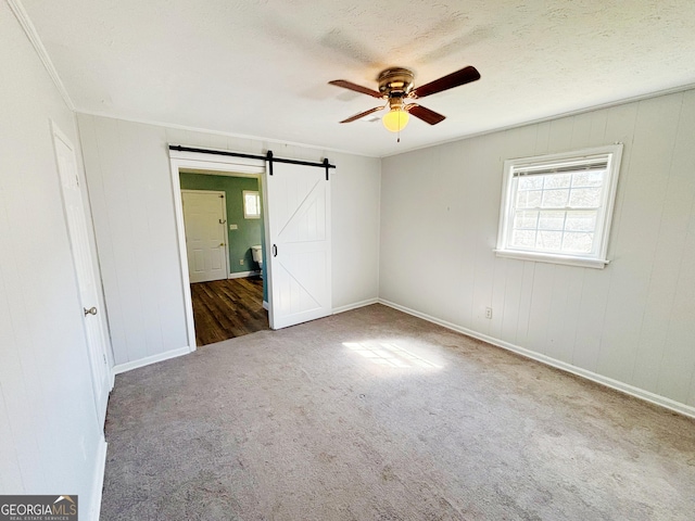 carpeted empty room with a textured ceiling, crown molding, ceiling fan, and a barn door