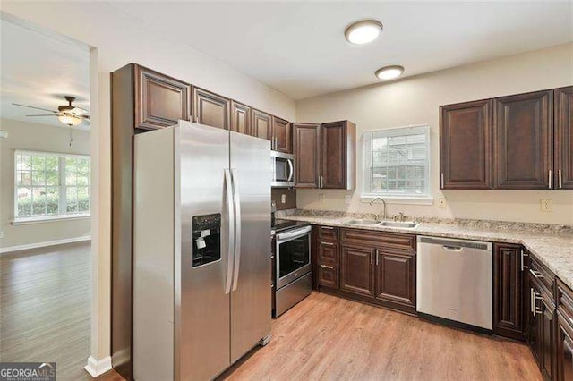 kitchen with appliances with stainless steel finishes, sink, light hardwood / wood-style flooring, light stone counters, and dark brown cabinets