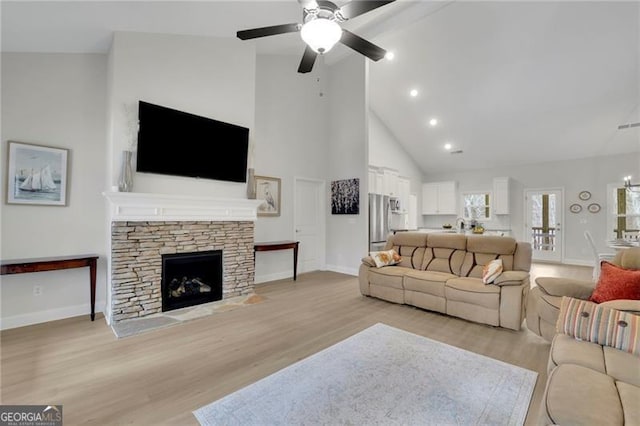 living room with a fireplace, ceiling fan, light hardwood / wood-style floors, and high vaulted ceiling