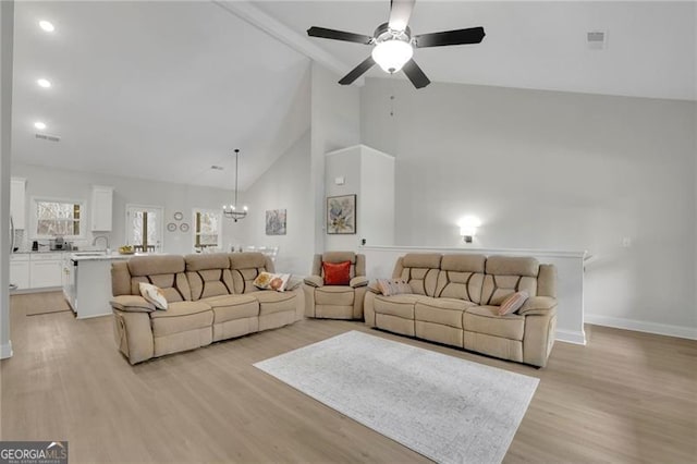 living room featuring ceiling fan with notable chandelier, light hardwood / wood-style flooring, and high vaulted ceiling