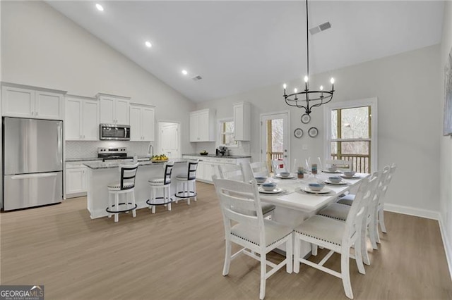 dining room featuring a notable chandelier, high vaulted ceiling, light hardwood / wood-style floors, and sink