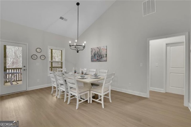 dining room featuring high vaulted ceiling, light wood-type flooring, and an inviting chandelier