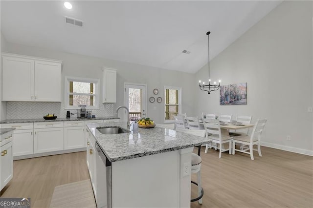 kitchen featuring a center island with sink, dishwasher, light stone counters, white cabinets, and decorative light fixtures