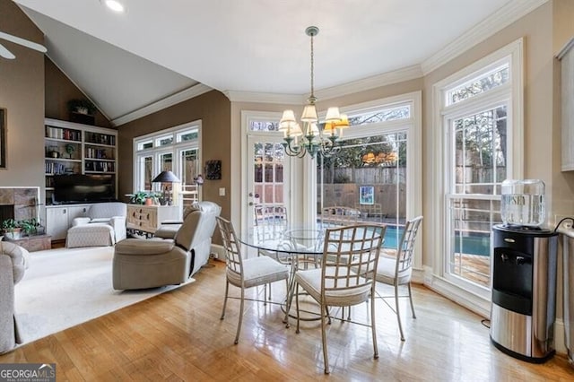 dining room with a chandelier, vaulted ceiling, light wood-type flooring, a fireplace, and ornamental molding