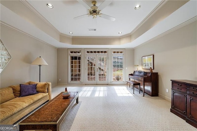 living area with a tray ceiling, ornamental molding, light colored carpet, and ceiling fan