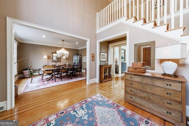 entrance foyer featuring a high ceiling, ornamental molding, a notable chandelier, and light hardwood / wood-style floors