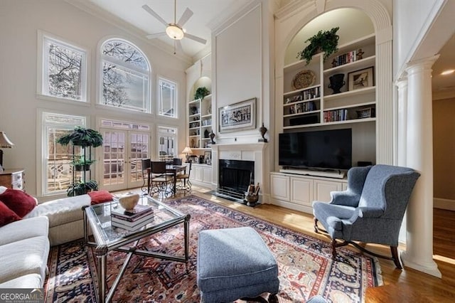 living room with built in shelves, ornamental molding, ornate columns, ceiling fan, and wood-type flooring