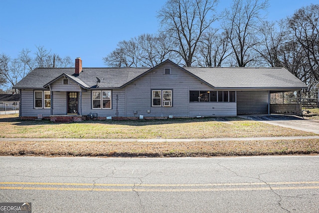 view of front of house featuring driveway, a shingled roof, a chimney, a front lawn, and a carport