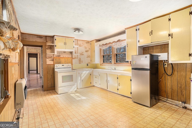 kitchen featuring heating unit, wood walls, white range with electric stovetop, freestanding refrigerator, and light floors