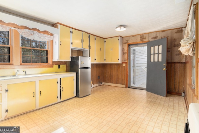 kitchen with wooden walls, a sink, light countertops, freestanding refrigerator, and light floors