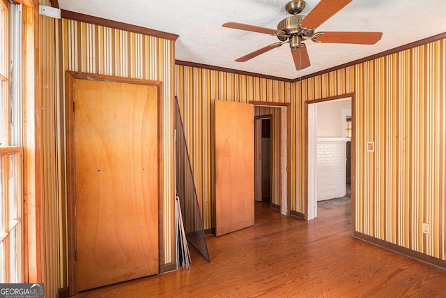 interior space featuring wallpapered walls, crown molding, a textured ceiling, and wood finished floors