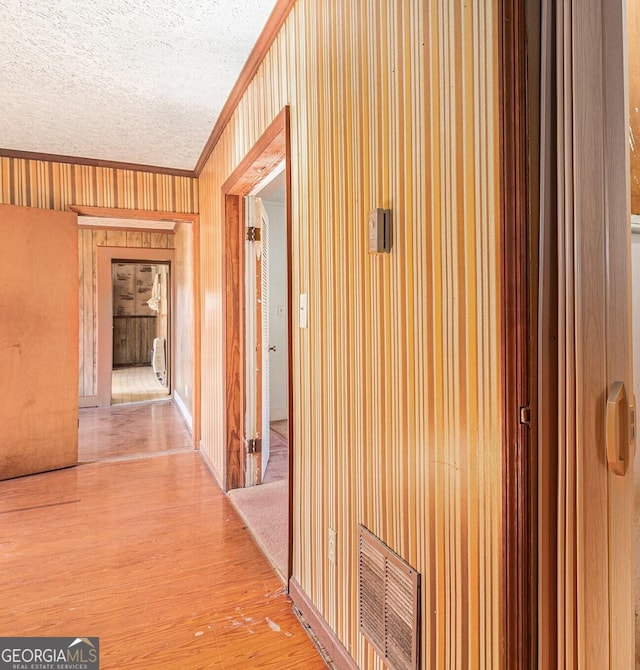 hallway with light wood-type flooring, visible vents, crown molding, and a textured ceiling