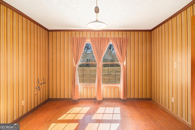 empty room featuring a textured ceiling, ornamental molding, wood finished floors, and baseboards